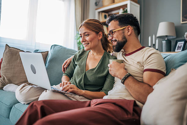 istock Happy couple relaxing on sofa browsing internet on laptop 2229583174