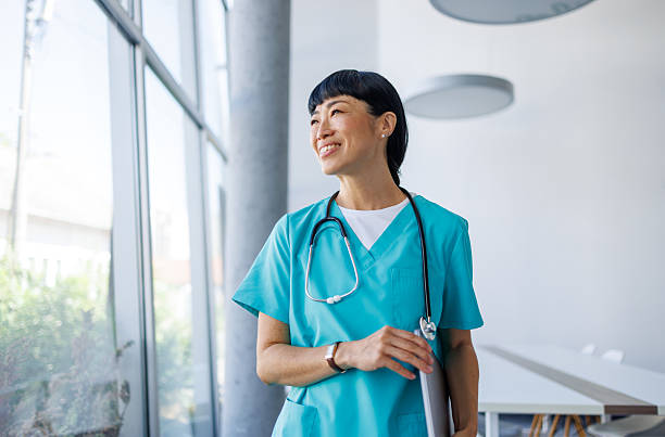 istock Smiling doctor looking out window in hospital corridor 2229583502