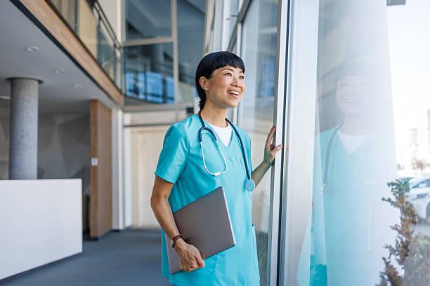 istock Smiling doctor looking through hospital window holding laptop 2229583594