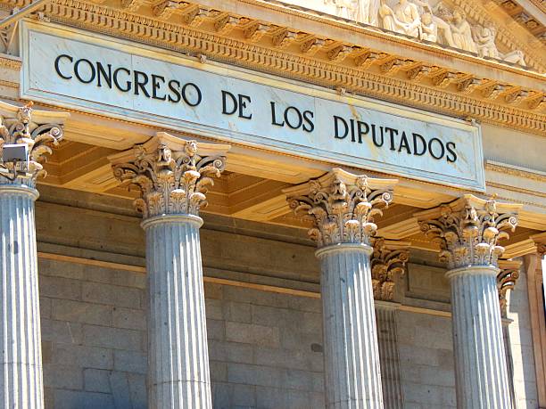 Night view of the Congress of Deputies (Congreso de los Diputados), the seat of the Spanish Parliament, illuminated against a dark sky in Madrid, Spain. The neoclassical facade, columns, and historic architecture are highlighted by warm lighting, representing Spanish politics, government, and democracy.