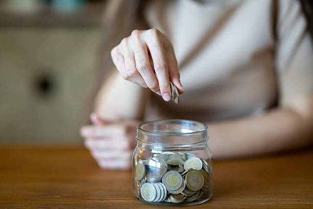 istock Woman saving money by dropping coins into glass jar 2229585335