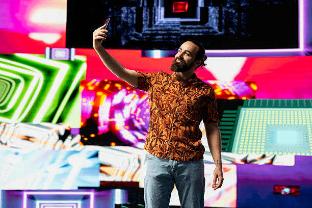 Cool relaxed man standing under neon lights with a smartphone, capturing photos and videos as a content creator and DJ. Confident carefree guy does visual art in a modern nightlife scene.