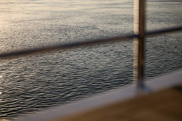 Calm water reflecting the warm hues of the setting sun viewed from behind a metal railing