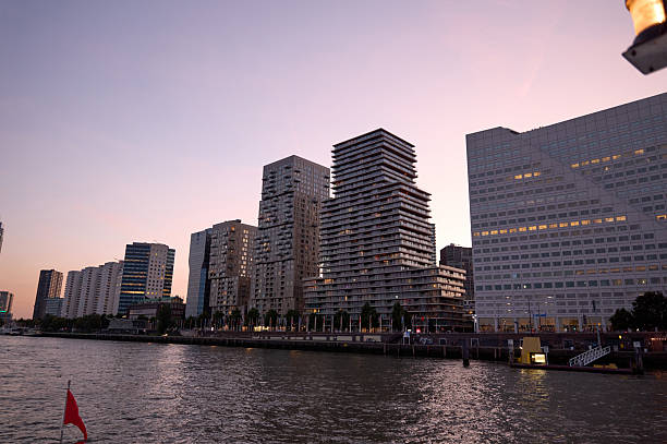 Modern buildings along the nieuwe maas river in rotterdam, netherlands, create a stunning cityscape at dusk