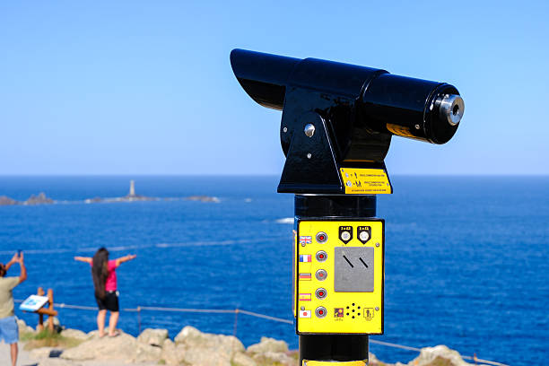 Shiny metallic binocular viewer on a scenic terrace overlooking the city. Blurred cityscape, sea and distant mountains create a colorful and inviting background perfect for travel themes