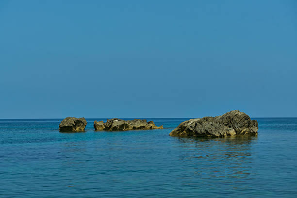 Tranquil seascape with rocks emerging from the calm blue ocean under a clear sky, capturing nature's serenity.