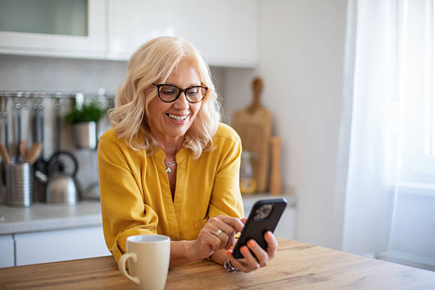 istock Senior woman using smartphone and smiling in kitchen 2229620600