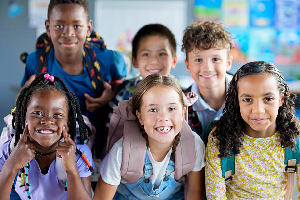 Kids of diverse backgrounds posing happily with backpacks in a vibrant and engaging classroom environment, symbolizing unity, joy, and the excitement of learning together.