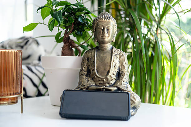 istock Buddha statue with smartphone on table surrounded by indoor plants 2229623900