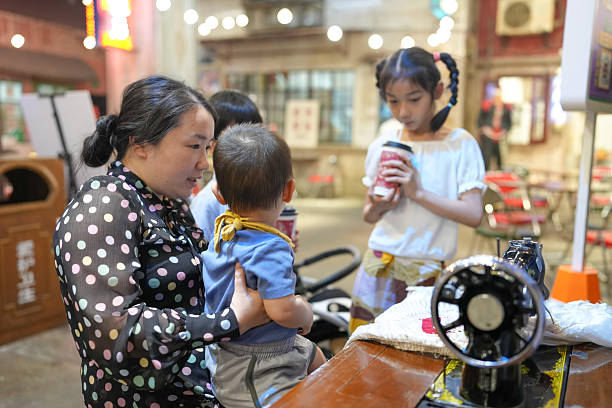 Inside an old-town mall, a Chinese family enjoys the day: a one-year-old in a stroller, kids under 10 laugh and chat as adults in their thirties use a vintage sewing machine. Shanghai, China. Spring.