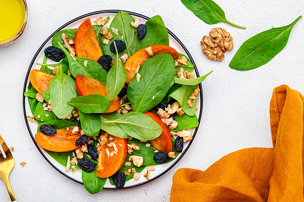 istock Yummy persimmon salad with walnuts, raisin and fresh spinach, white background, top view 2229650610