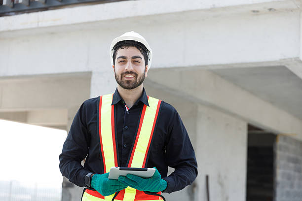 istock Confident construction engineer wearing safety vest and white helmet holding tablet at construction site, using digital tools for building inspection, project planning, and on site coordination. 2229651989