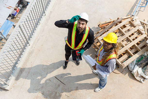 istock Two construction engineers wearing safety helmets and reflective vests discussing blueprints at building site, representing teamwork, planning. View from above. 2229652006