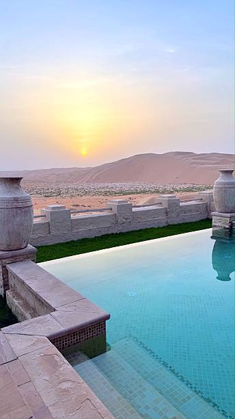 istock Luxurious infinity pool reflecting golden sunrise light, panoramic desert vista with undulating sand dunes and minimal greenery 2229655053