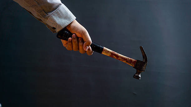 istock Man in long-sleeved shirt gripping hammer's black rubber handle, black background, ideal for repair, construction, or handyman concepts. 2229661853