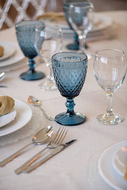 istock Plates stacked on textured glass chargers, blue tinted goblets with a diamond-cut pattern alongside white wine glasses 2229682060