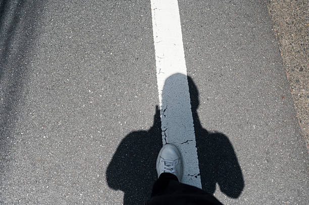 Shadow and foot over white street line on asphalt road in daylight.