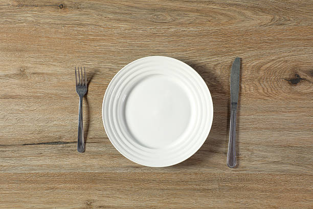 istock One empty round white ceramic plate with fork and knife on wooden table 2229682776