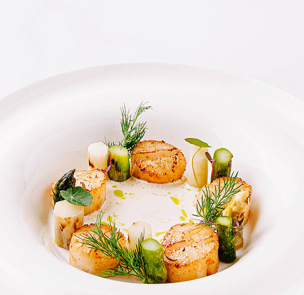 istock Deliciously prepared scallops with fresh herbs and vegetables on a white plate 2229682835