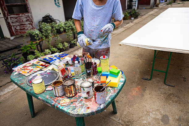A male artist in a work suit prepares paints for creation in an outdoor studio.