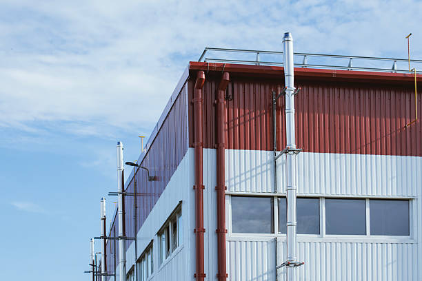 Contemporary industrial facility exterior featuring a red and white metal panel facade with silver exhaust or ventilation pipes. Concept modern industrial architecture