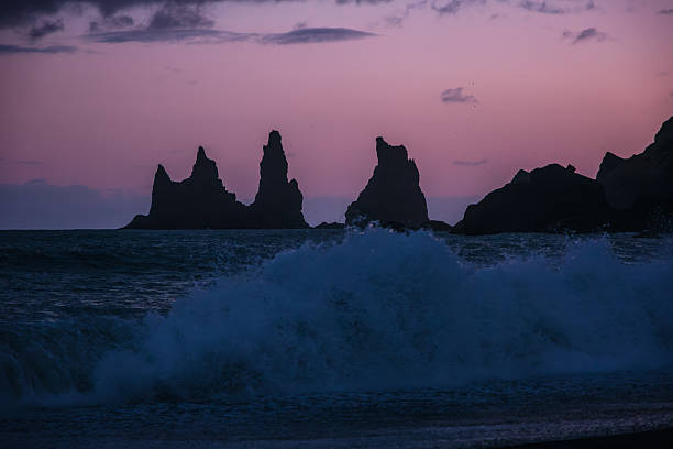 The dramatic Reynisdrangar basalt sea stacks rising through breaking waves seen from Vikurfjara beach on Iceland's wild south coast during sunset
