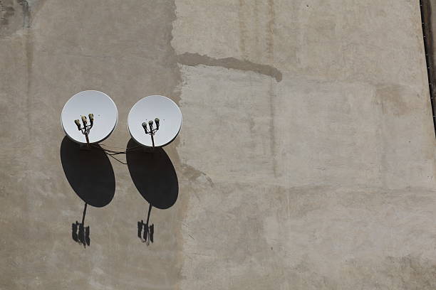 Satellite dishes mounted on a concrete wall casting distinct shadows in bright sunlight