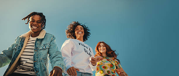 Three stylish young friends laughing and walking together under a clear sky. Emphasizes freedom, social connection, and the vibrant energy of modern youth culture.