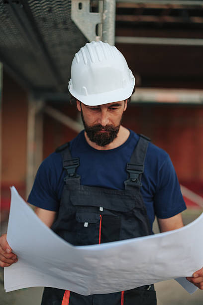 istock Construction worker reading blueprints on site wearing hardhat and overalls 2229728403
