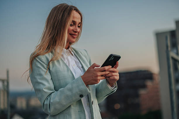 istock Businesswoman using smartphone on rooftop at sunset 2229728487