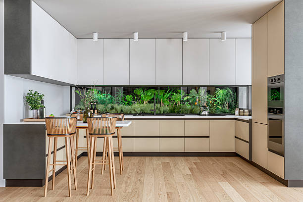 istock A modern kitchen with  muted beige (nude) and white cabinetry, lush indoor green wall as backsplash, a bar-height dining area with wooden stools on hardwood floor 2229729700