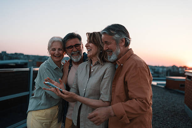istock Four seniors enjoying sunset on rooftop, laughing and taking photos 2229735525