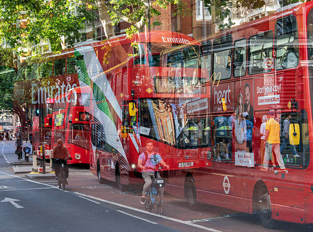 London, United Kingdom - June 24, 2025: A busy London street with iconic red double-decker buses and a cyclist in motion, reflecting urban life and transportation.