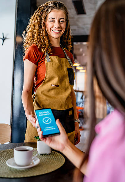 Smiling waitress accepting mobile payment from customer in coffee shop