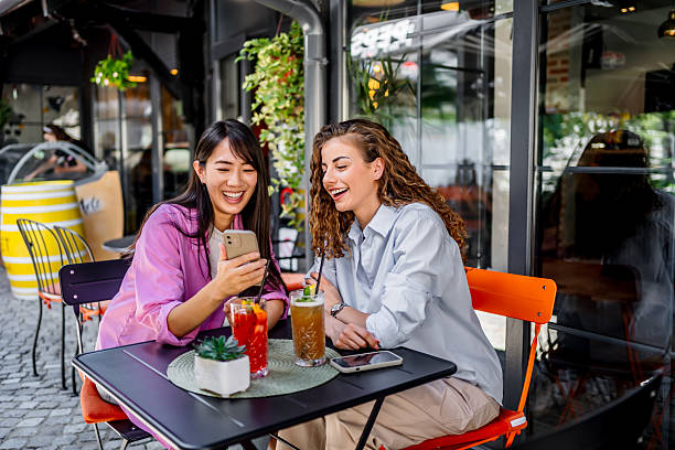 istock Two young women laughing while looking at smartphone in outdoor cafe 2229739744