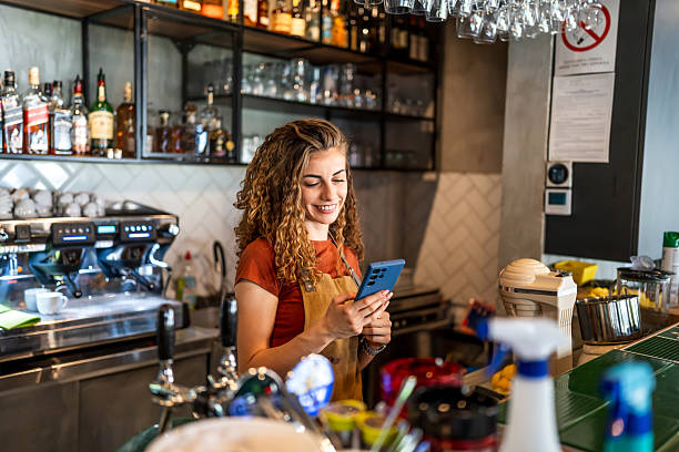 istock Smiling barista using smartphone behind counter in modern cafe 2229739934