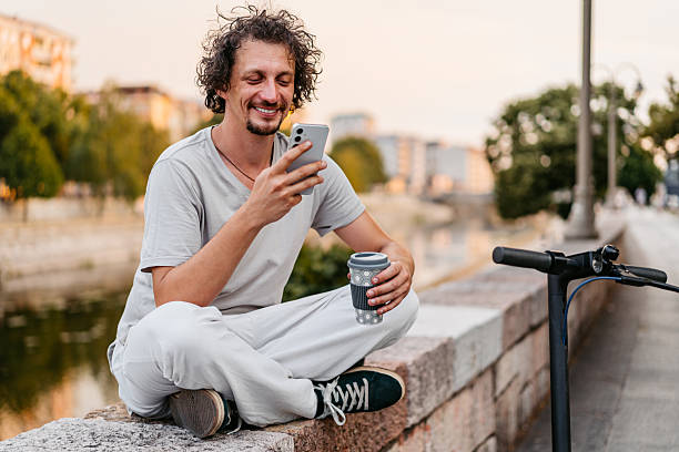 istock Mid-Adult Man With An Electric Scooter Using Phone While Drinking Coffee On The Quayside 2229740775