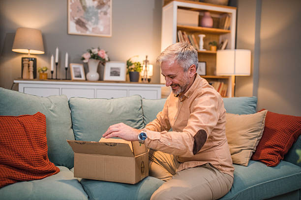 istock Excited man unboxing package he ordered online while sitting on sofa in living room 2229741069