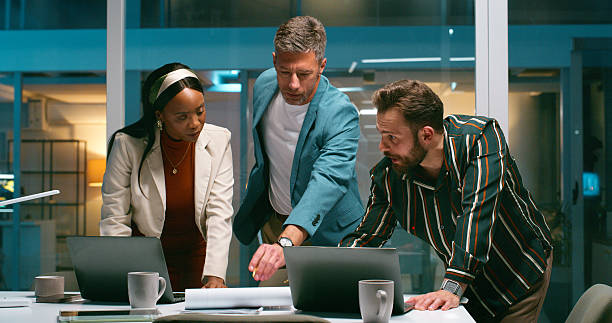 istock People, meeting and document in office at night for planning, article feedback and press release. Staff, team and laptop for proofreading, headline solution and brainstorming for publication deadline 2229742477