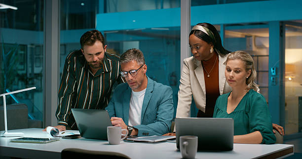 istock Business people, night or collaboration with laptop in office for project deadline or development. Group, employee or team working late with computer or technology for performance review in workplace 2229742500