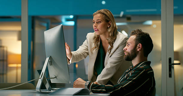 istock Computer, help and business people in office, night and financial agency with feedback. Evening, coaching and employees in workplace, pc and mentor with discussion, accounting or review budget report 2229745732