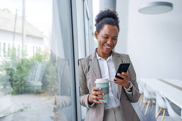 istock Smiling businesswoman using smartphone and drinking coffee during break 2229747981