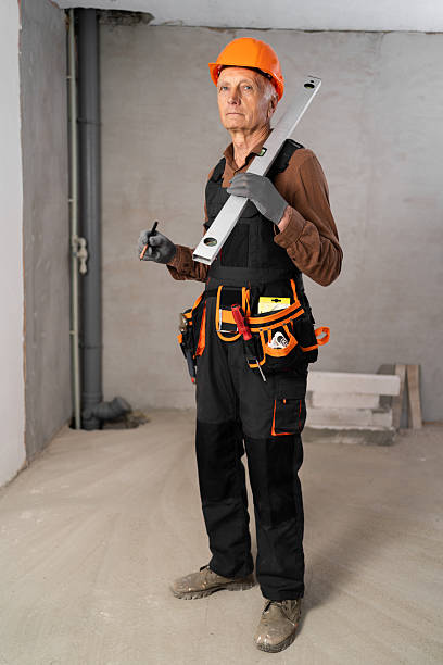 istock Elderly builder with tool belt holding wall measuring level and pencil looking at camera kindly. House construction and renovation 2229749894