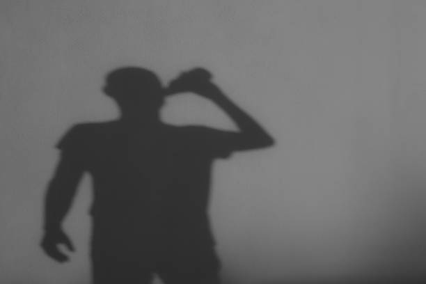 istock Shadow figure. A man drinks alcohol from a bottle. Back view of shadow. Alcohol Abuse 2229750471