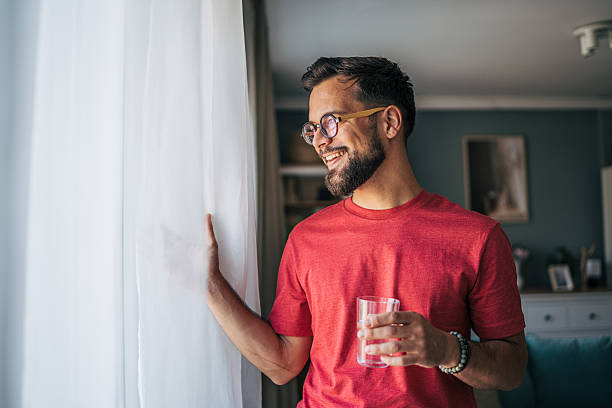 Smiling man drinking water and looking out the window at home