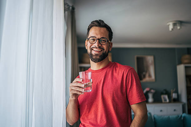 istock Young man smiling and drinking water at home 2229750959