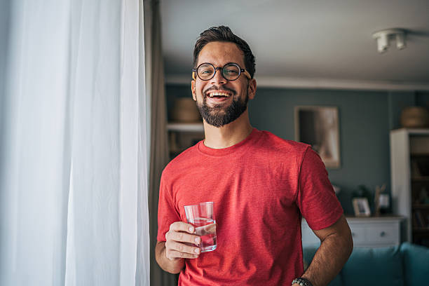istock Young man smiling and drinking water at home 2229750962