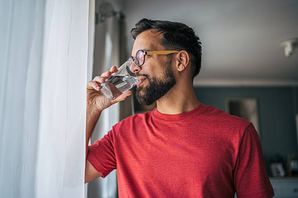 istock Man drinking water glass near window at home 2229750984