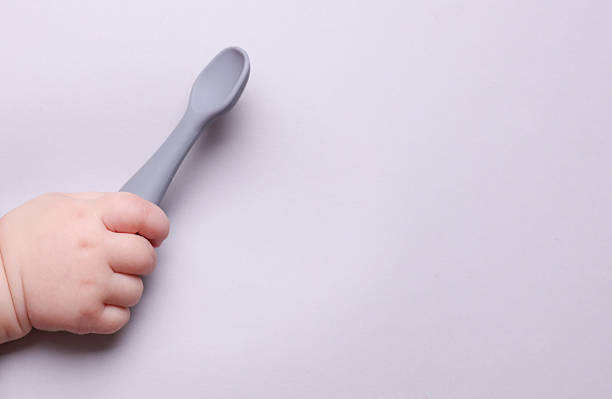 istock Baby hand holding silicone feeding spoon on gray background 2229752014