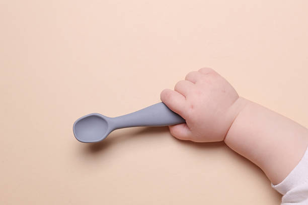 istock Baby hand holding silicone feeding spoon on beige background 2229752015
